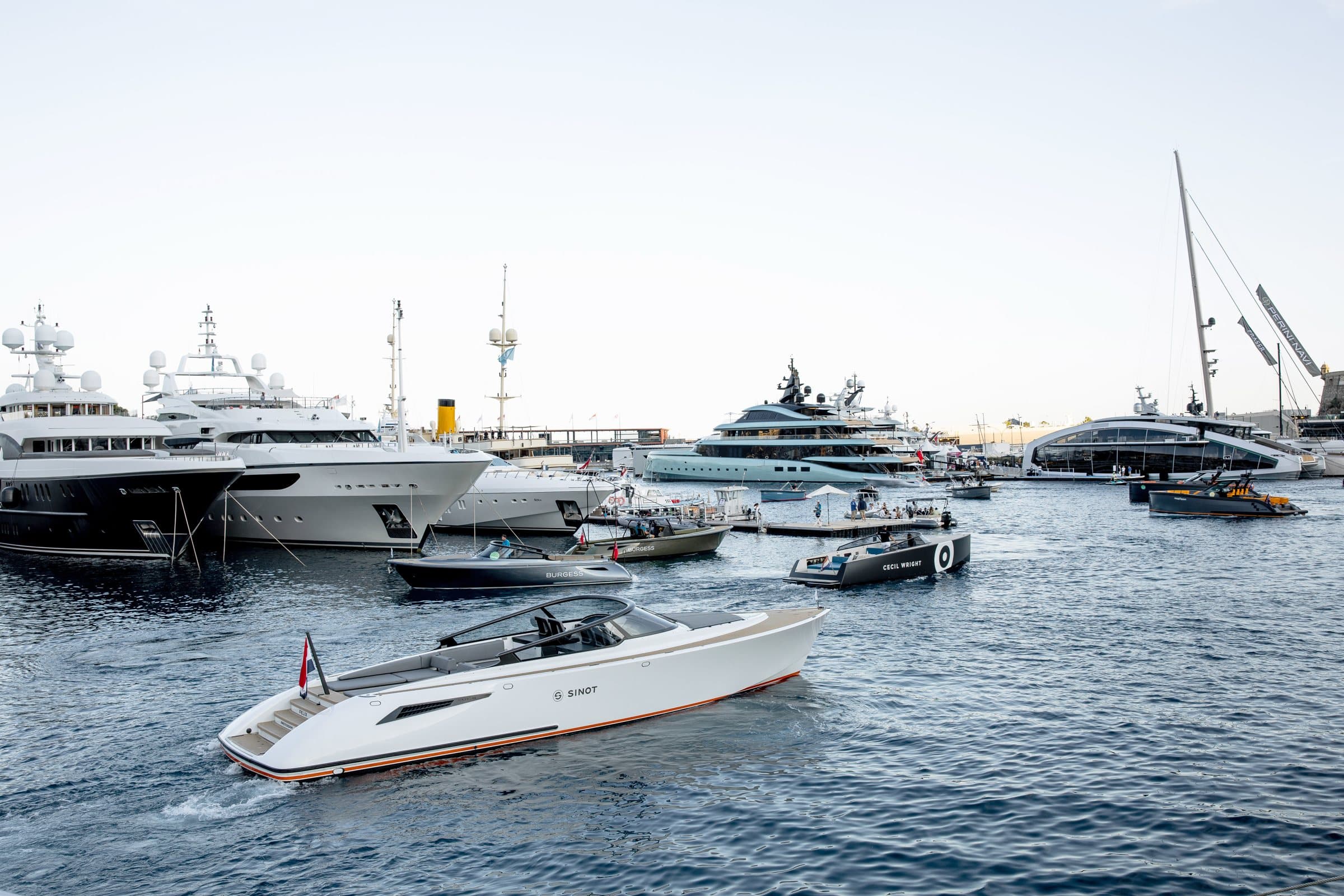 Tenders crossing Monaco harbour at golden hour, superyachts berthed along the quay behind